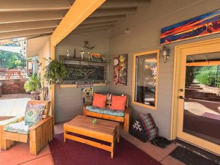 A colorful and artistic porch with a bright orange cushioned bench, chalkboard menu, and various decorative items on the walls